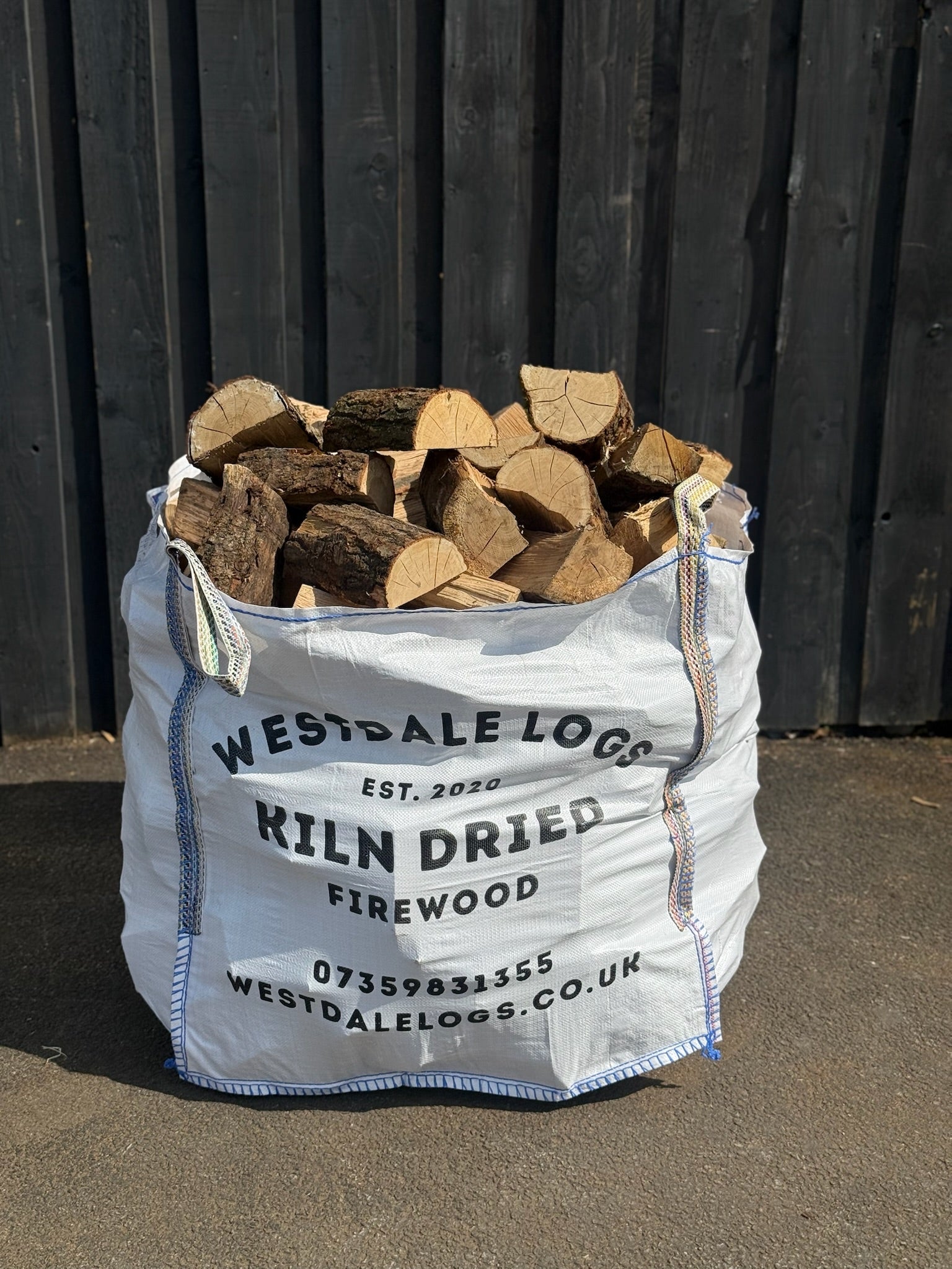 Bag of kiln dried oak firewood from Westdale Logs against a wooden fence.