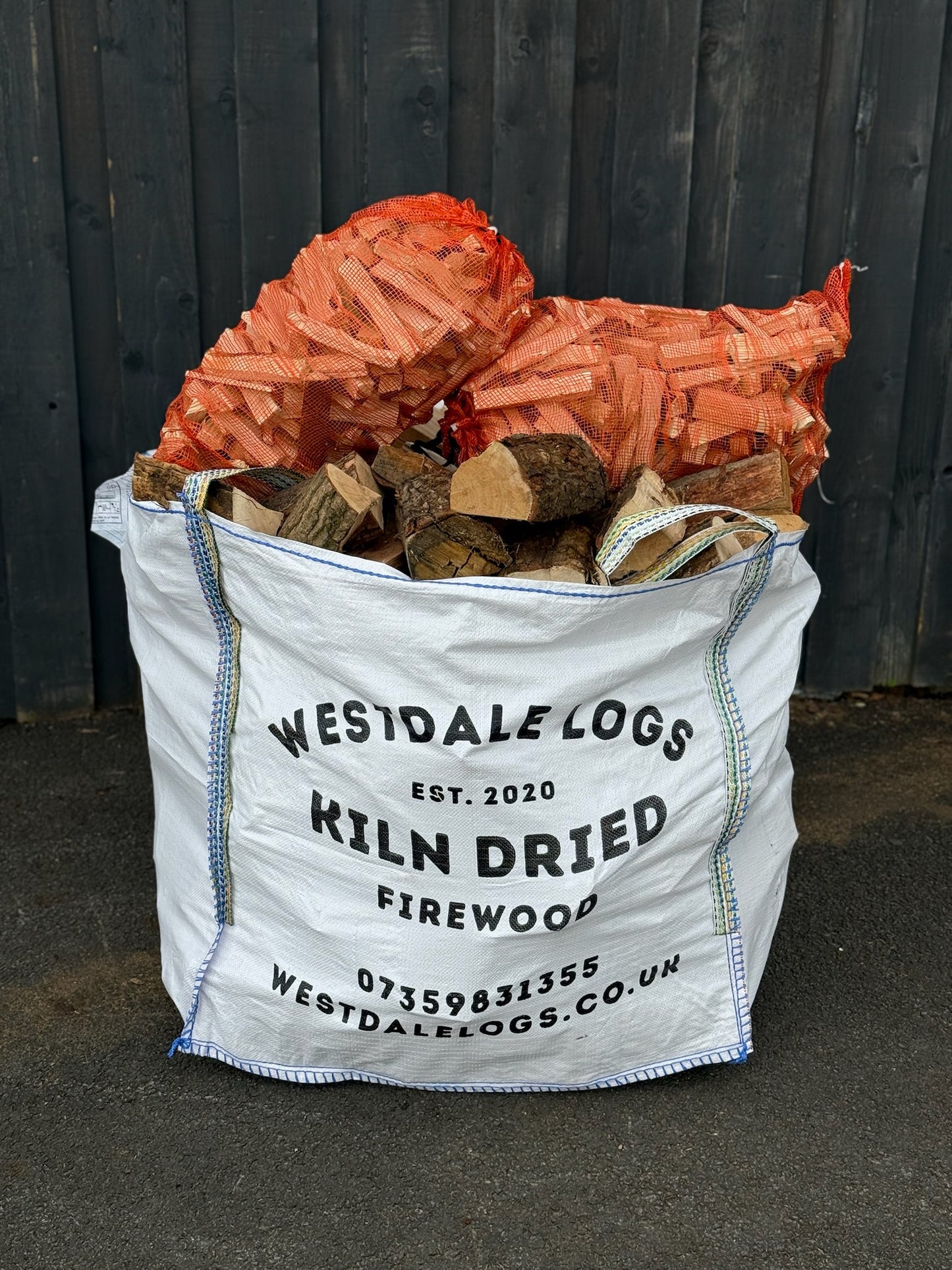 Bag of Westdale Logs kiln dried Oak firewood with visible branding and contact information. The bulk bag also has two nets of kindling placed upon it